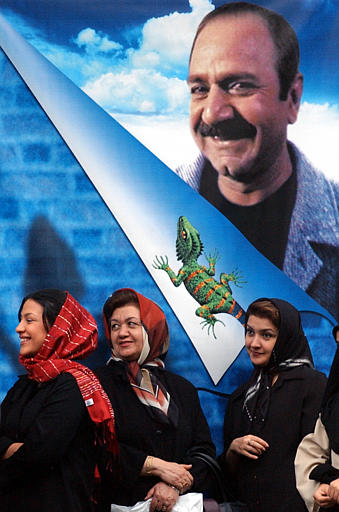Iranian women wait to buy tickets for 'Marmulak' (The Lizard) under a poster of Iranian actor Parviz Parastui, in scenes from the film, directed by Manuchehr Mohammadi, outside a cinema in central Tehran, May 1, 2004.